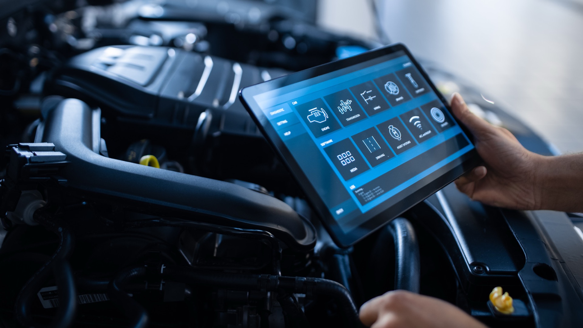 Technician holding a tablet running a vehicle diagnostics application over an open engine bay